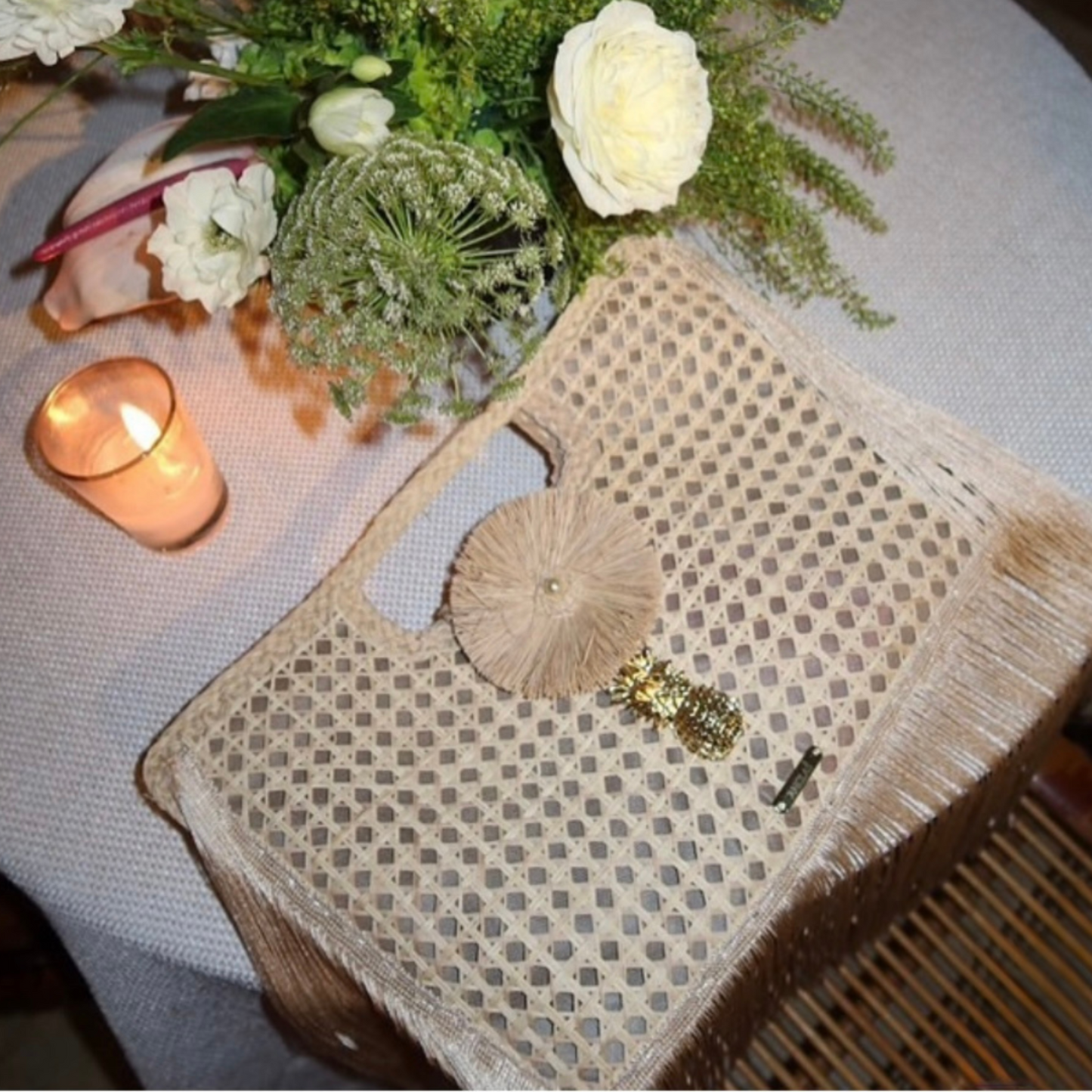 Woven clutch bag on a table with flowers and a candle